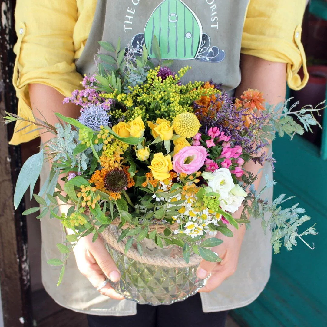 Cute mini lantern absolutely bursting with life and colour, containing an assortment of bright flowers such as roses, lisianthus, september flower, bouvardia, and craspedia.