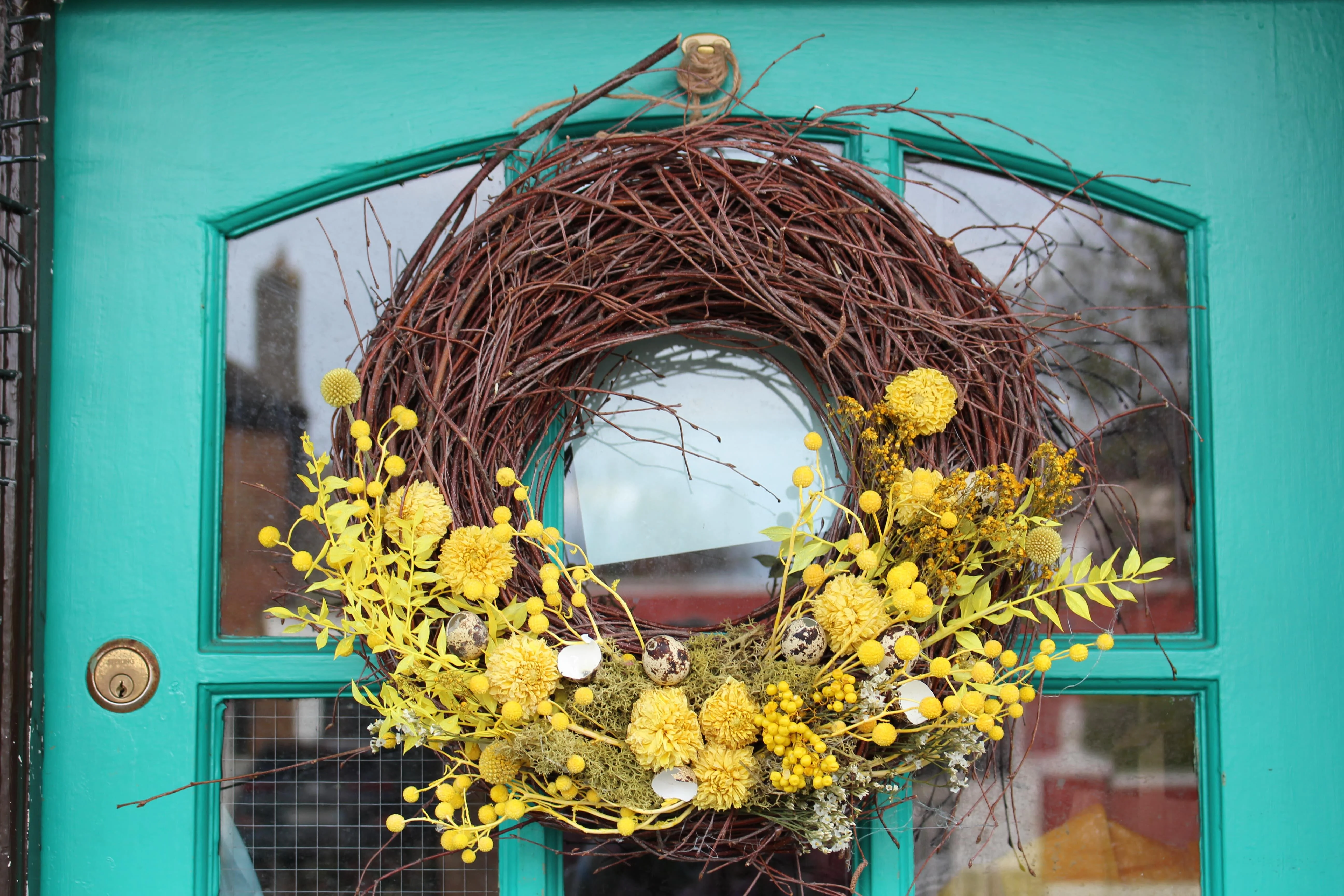 Rustic Easter wreath combining large bundles of intertwined twigs and generous helpings of bright yellow dried flowers.