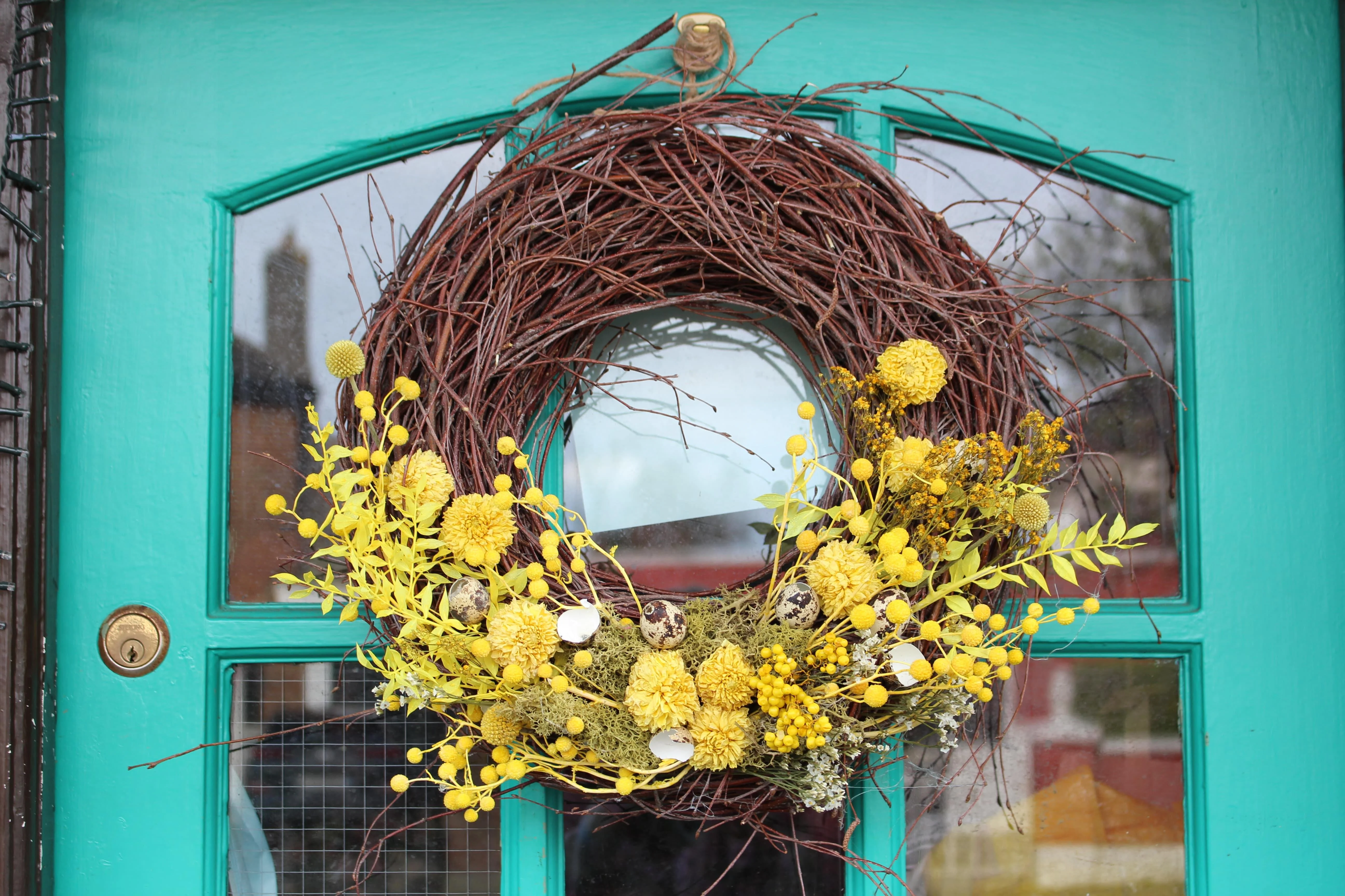 Rustic Easter wreath combining large bundles of intertwined twigs and generous helpings of bright yellow dried flowers.
