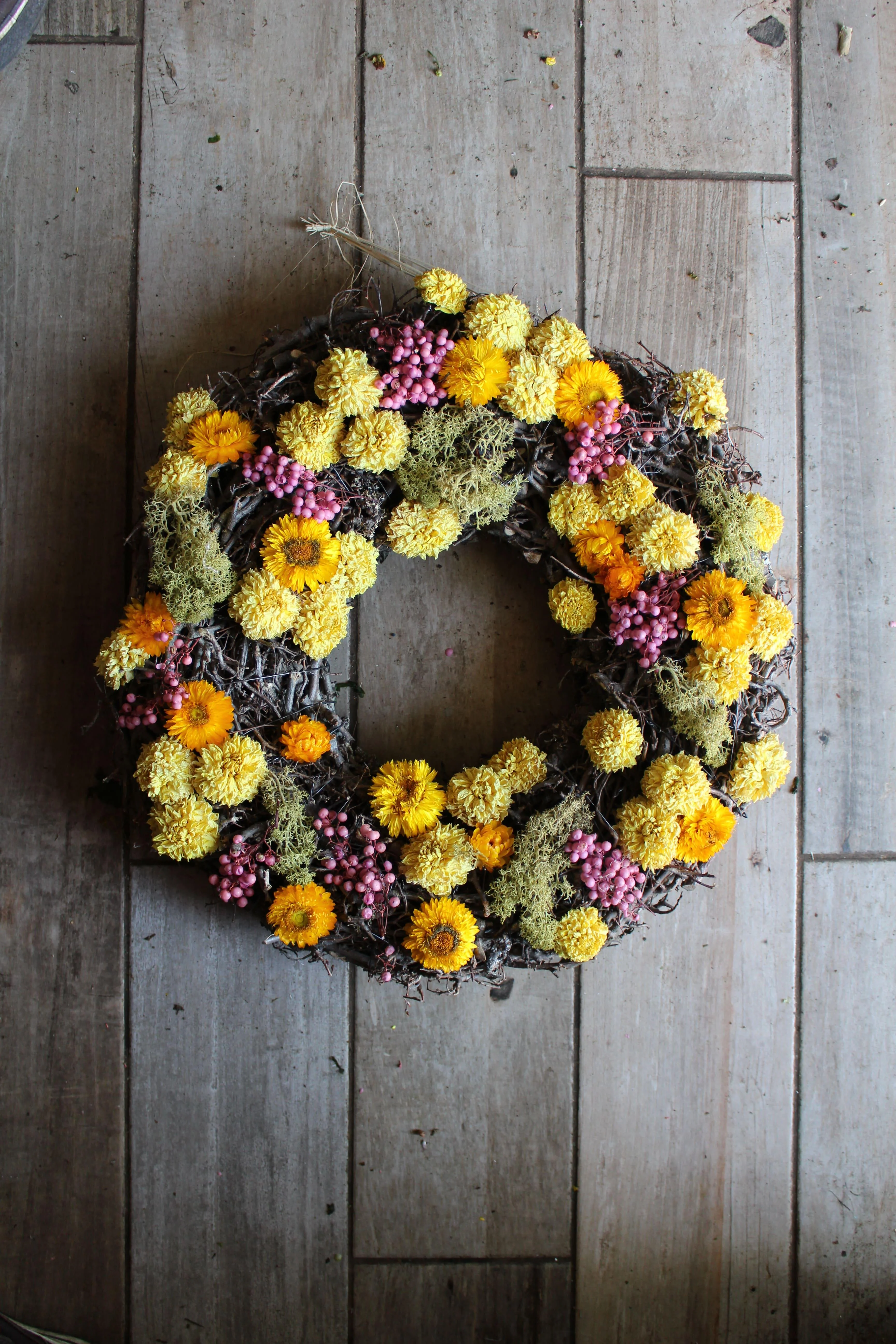 Pretty yellow wreath formed from a base of intertwined twigs and reindeer moss adorned with bright yellow and lipstick pink dried flowers - a spring themed wreath perfect for Easter.
