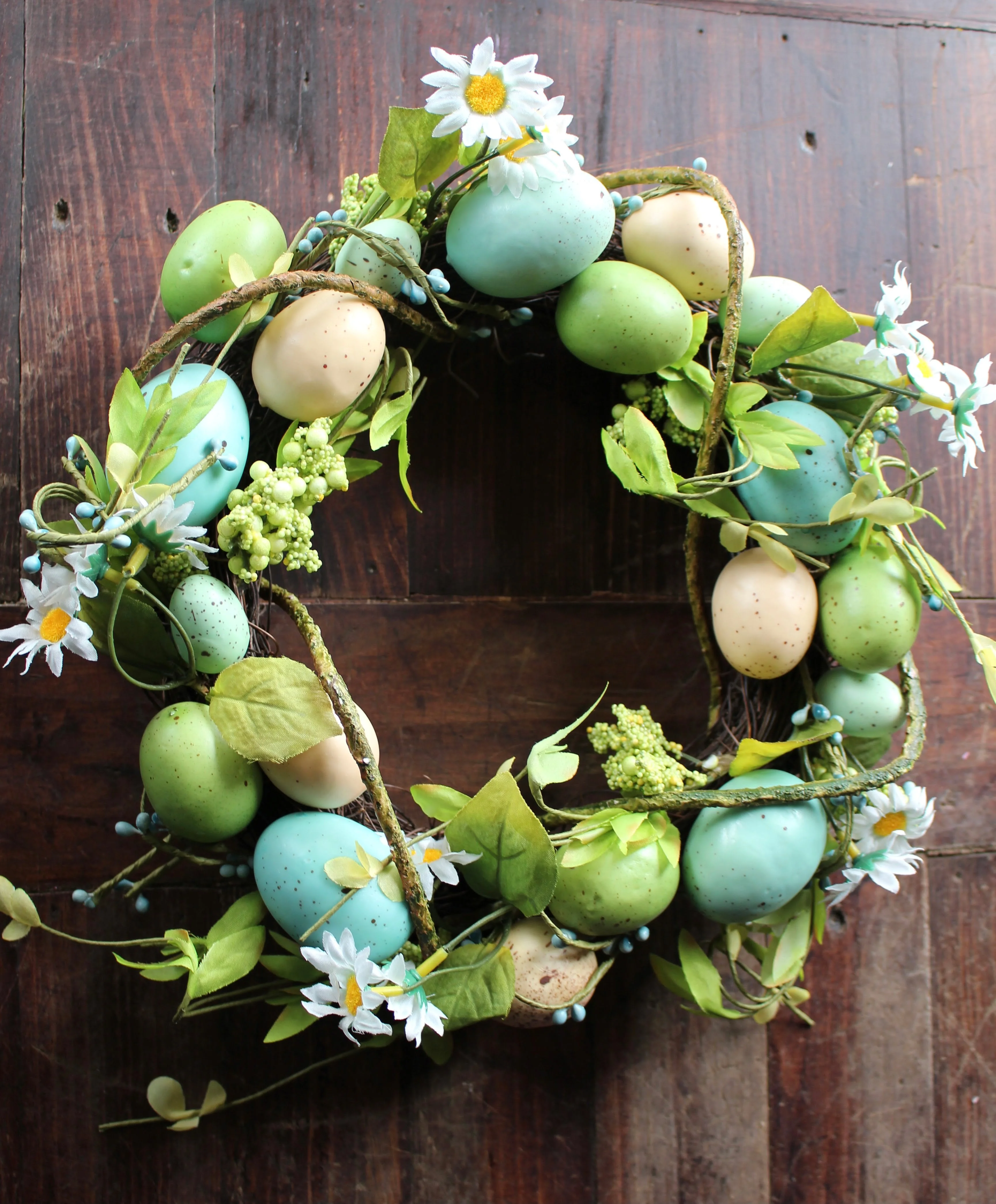 Pretty artificial Easter egg wreath combining pastel coloured Easter eggs with vines and daisy like flowers.