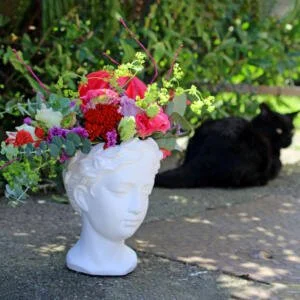 Elegant goddess themed plant pots featuring serene faces reminiscent of greek sculptures, filled with whatever gorgeous flowers we have available each week.