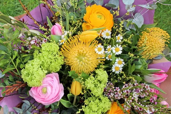 Beautiful spring themed floral bouquet featuring large, bright yellow and pink blooms mixed with cute little meadow flowers and lots of lush greenery.